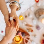 Hands exchanging energy with crystals and candles on a mystic table setting.
