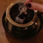 Close-up of a hand burning sage over an aroma lamp for relaxation indoors.