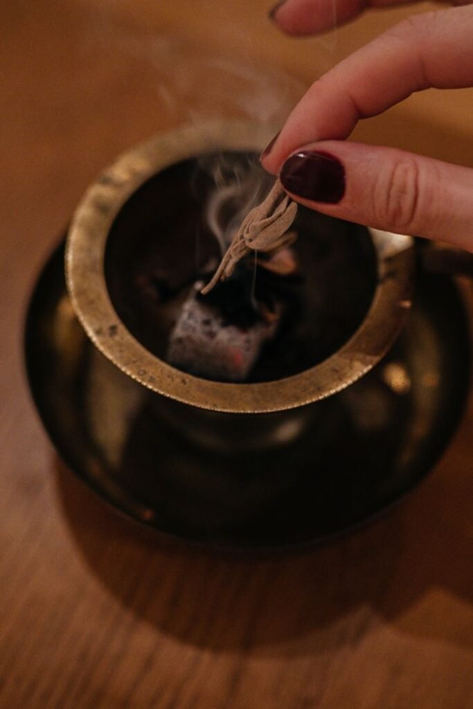 Close-up of a hand burning sage over an aroma lamp for relaxation indoors.